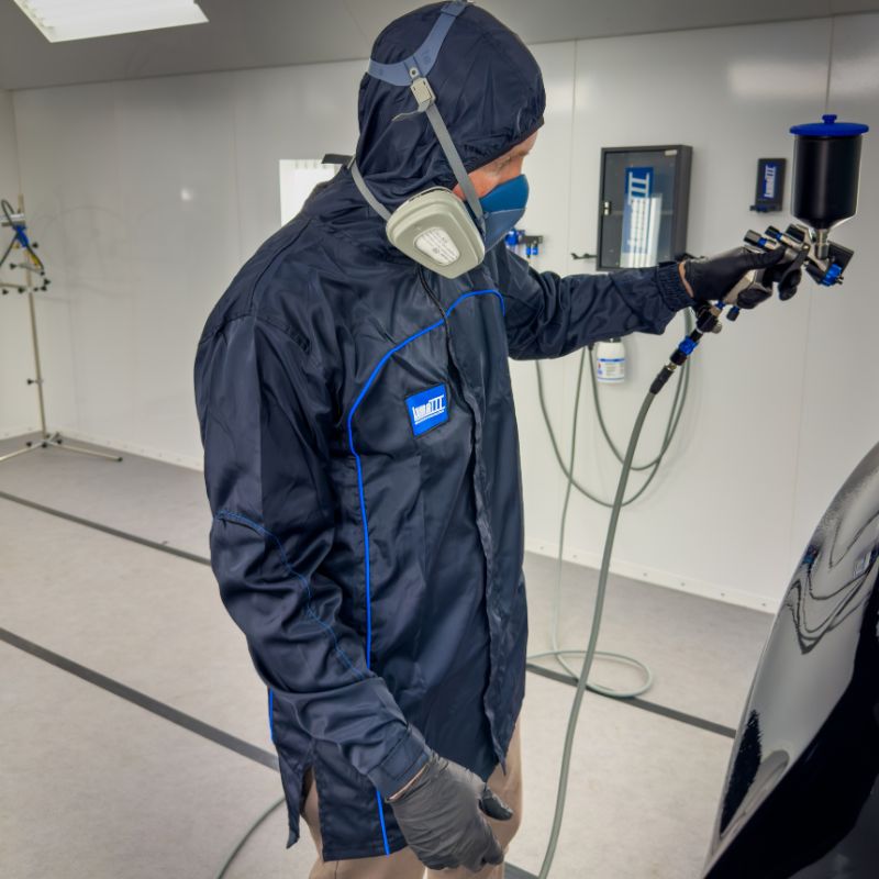 Person in a spray booth wearing Luma III Lab Coat and spraying a car.
